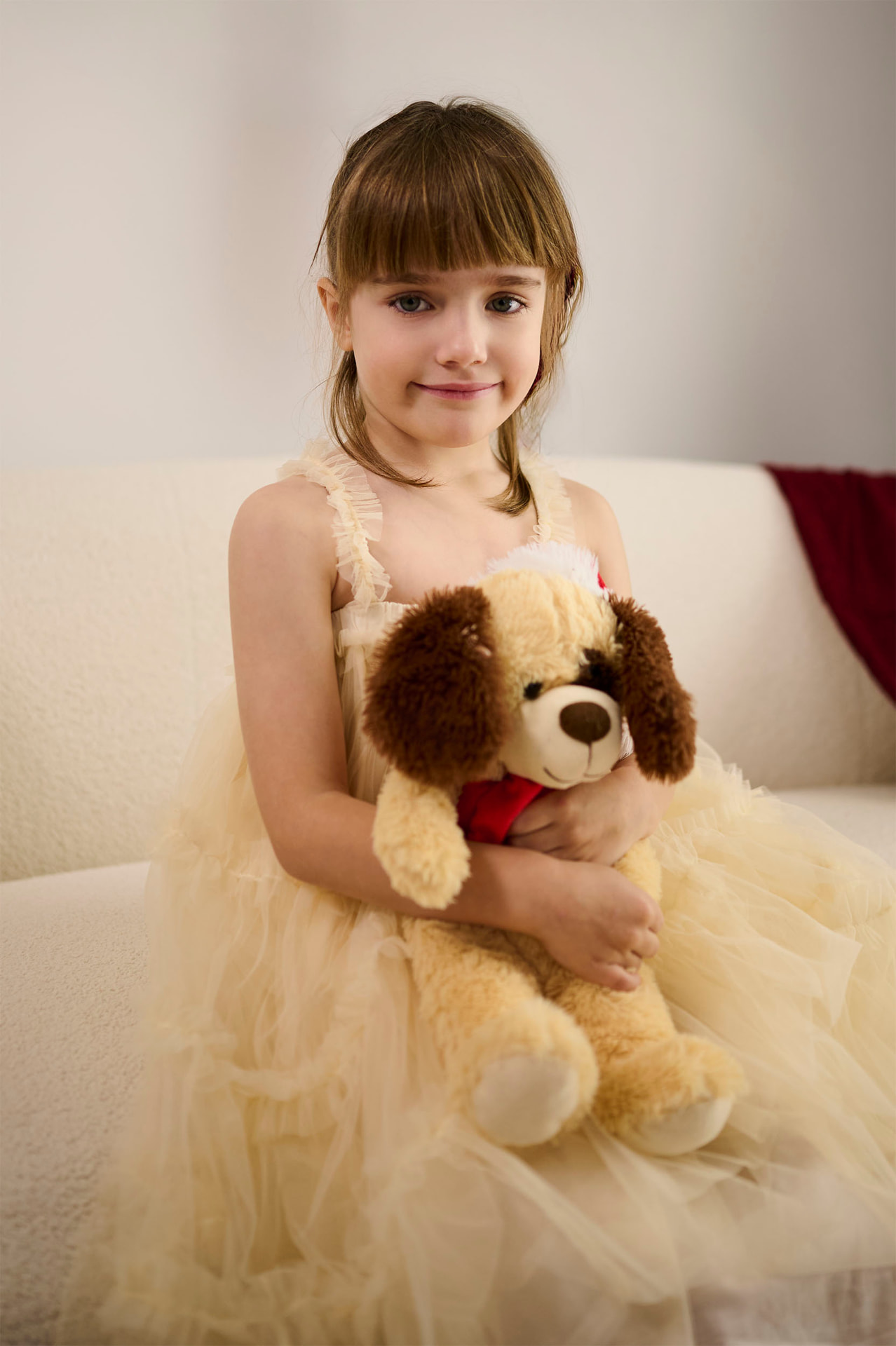 Young girl in a cream dress holding a soft toy in the studio