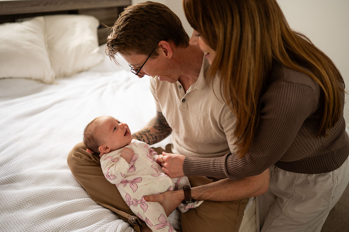 A mother and father smiling down at their newborn baby on a bed at home